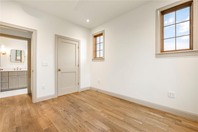 unfurnished bedroom featuring light hardwood / wood-style floors, sink, multiple windows, and ceiling fan