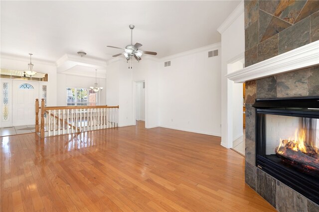 living room featuring a tiled fireplace, crown molding, hardwood / wood-style floors, and ceiling fan with notable chandelier