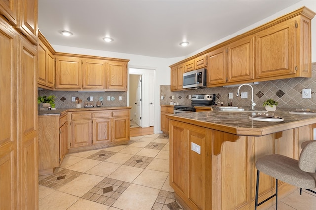 kitchen with a kitchen bar, kitchen peninsula, stainless steel appliances, sink, and light tile patterned flooring