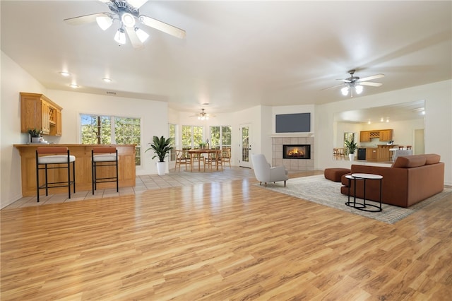 living room featuring ceiling fan, light wood-type flooring, and a tiled fireplace