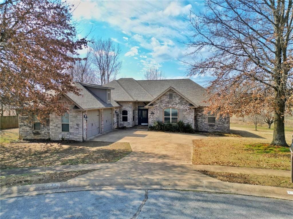 view of front of house featuring a shingled roof, a front yard, a garage, stone siding, and driveway