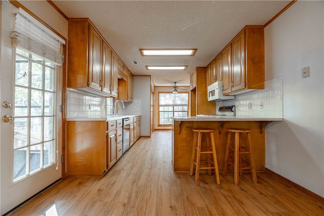 kitchen with a textured ceiling, kitchen peninsula, light hardwood / wood-style floors, and white appliances