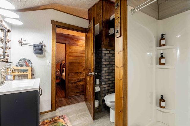 bathroom with toilet, vaulted ceiling, a textured ceiling, hardwood / wood-style flooring, and vanity