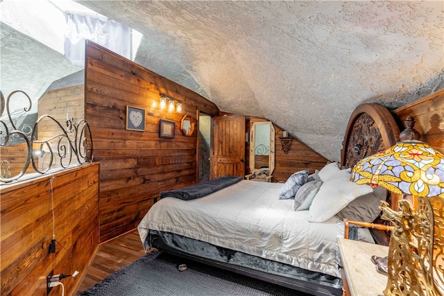 bedroom with hardwood / wood-style floors, wood walls, a textured ceiling, and lofted ceiling