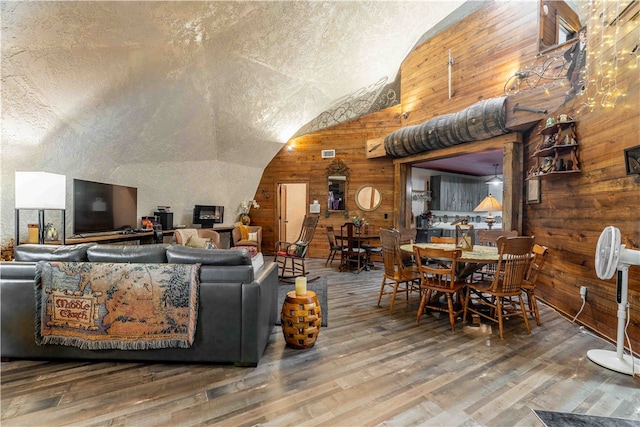 living room with wooden walls, hardwood / wood-style floors, vaulted ceiling, and a textured ceiling