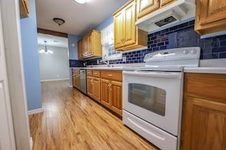 kitchen featuring dishwasher, a notable chandelier, light wood-type flooring, white electric stove, and decorative backsplash