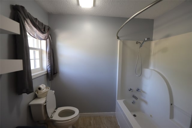 bathroom with a textured ceiling, hardwood / wood-style floors, toilet, and washtub / shower combination