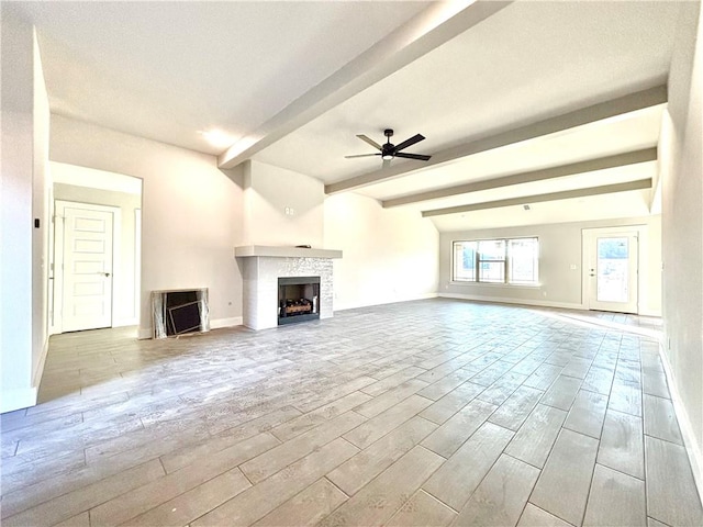 unfurnished living room with beamed ceiling, ceiling fan, and a stone fireplace