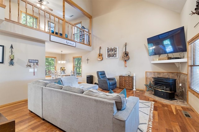 living room featuring ceiling fan with notable chandelier, hardwood / wood-style floors, a wood stove, and a high ceiling