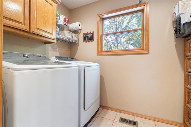 clothes washing area featuring light tile patterned flooring, separate washer and dryer, and cabinets