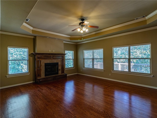 unfurnished living room featuring crown molding, plenty of natural light, a tray ceiling, and dark hardwood / wood-style flooring