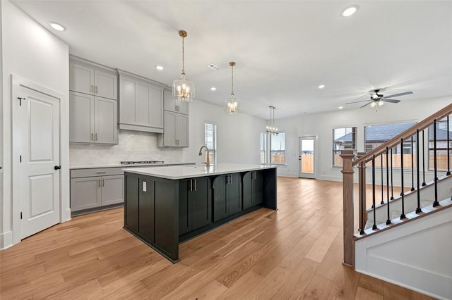 kitchen featuring gray cabinets, an island with sink, backsplash, hanging light fixtures, and light hardwood / wood-style flooring