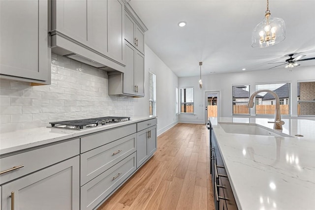 kitchen featuring premium range hood, sink, stainless steel gas cooktop, gray cabinetry, and pendant lighting