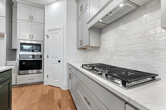 kitchen with stainless steel appliances, gray cabinetry, backsplash, and light hardwood / wood-style floors