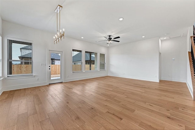 unfurnished living room featuring ceiling fan with notable chandelier and light wood-type flooring