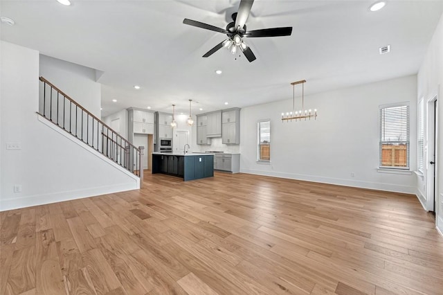 unfurnished living room featuring ceiling fan with notable chandelier, sink, light hardwood / wood-style floors, and a wealth of natural light