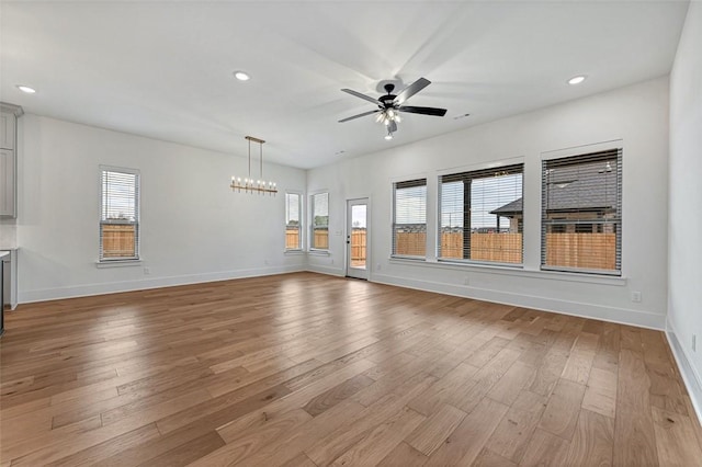 unfurnished living room with ceiling fan with notable chandelier and light hardwood / wood-style floors