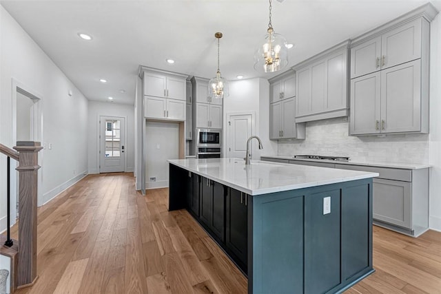 kitchen with hanging light fixtures, an island with sink, sink, and gray cabinets