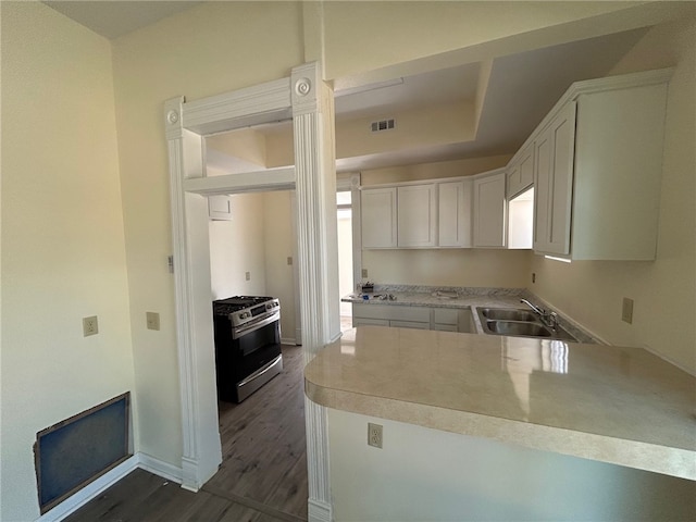 kitchen featuring kitchen peninsula, sink, stainless steel gas range, and white cabinetry