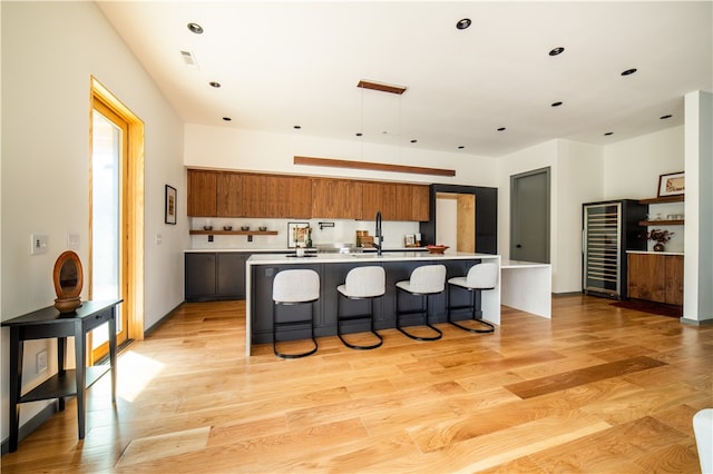 kitchen with a kitchen bar, an island with sink, light hardwood / wood-style floors, and beverage cooler