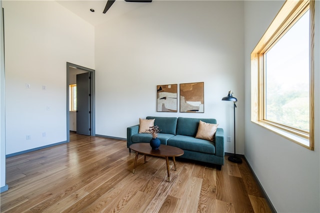 living room featuring ceiling fan, a towering ceiling, and light hardwood / wood-style floors