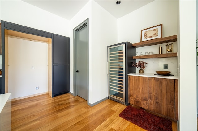 bar with wine cooler, decorative backsplash, and light wood-type flooring