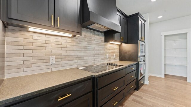 kitchen featuring wall chimney range hood, light hardwood / wood-style floors, decorative backsplash, stainless steel oven, and black electric cooktop