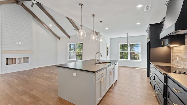 kitchen with tasteful backsplash, a kitchen island with sink, vaulted ceiling with beams, wall chimney exhaust hood, and sink