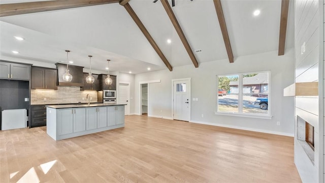 kitchen featuring backsplash, hanging light fixtures, an island with sink, stainless steel appliances, and high vaulted ceiling