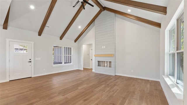 unfurnished living room with beam ceiling, a large fireplace, light hardwood / wood-style floors, and high vaulted ceiling