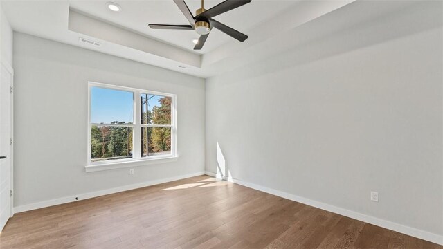 spare room with ceiling fan, hardwood / wood-style floors, and a raised ceiling