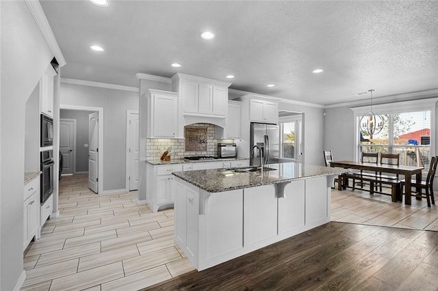 kitchen with white cabinets, a kitchen island with sink, stainless steel appliances, light hardwood / wood-style floors, and sink