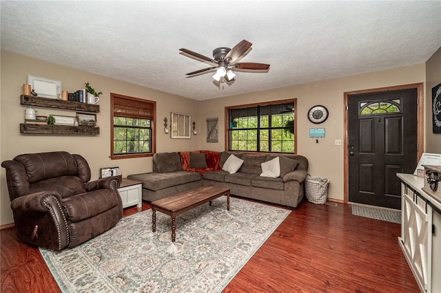 living room featuring dark wood-type flooring, ceiling fan, and a textured ceiling