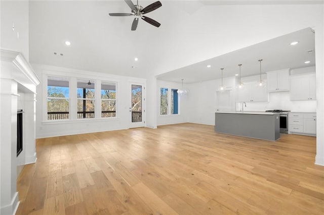 unfurnished living room with vaulted ceiling, ceiling fan with notable chandelier, light hardwood / wood-style flooring, and sink