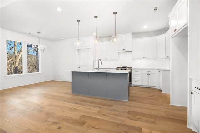 kitchen with an island with sink, hanging light fixtures, stainless steel stove, white cabinets, and sink