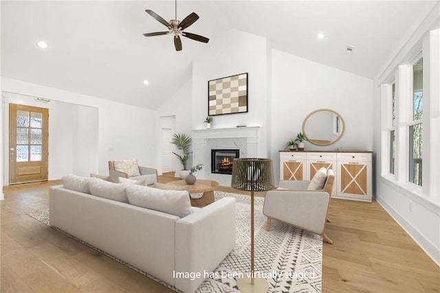 living room with high vaulted ceiling, light wood-type flooring, a high end fireplace, and ceiling fan