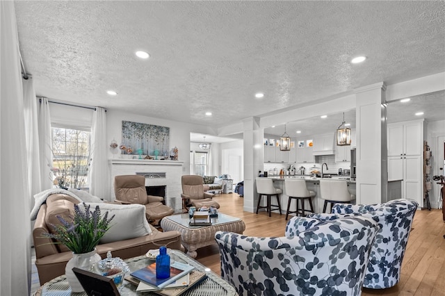 living room with a textured ceiling, sink, and light wood-type flooring