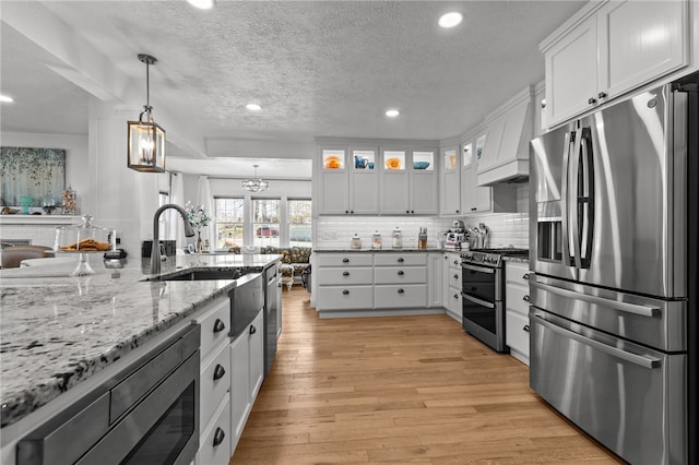 kitchen with custom exhaust hood, white cabinetry, stainless steel appliances, and light hardwood / wood-style floors