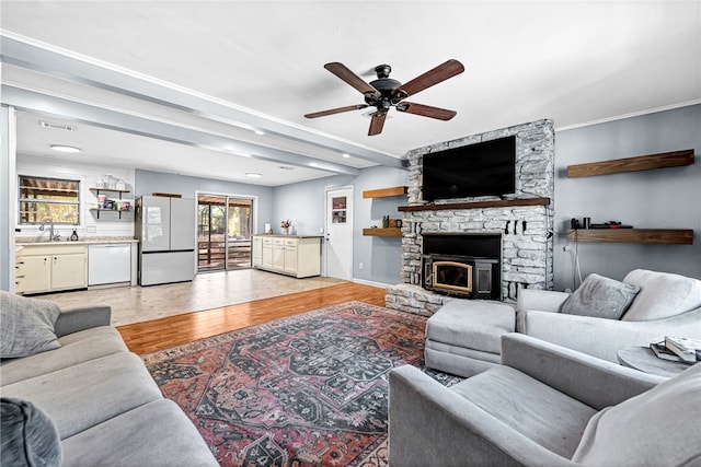 living room featuring light hardwood / wood-style floors, a stone fireplace, sink, and ceiling fan