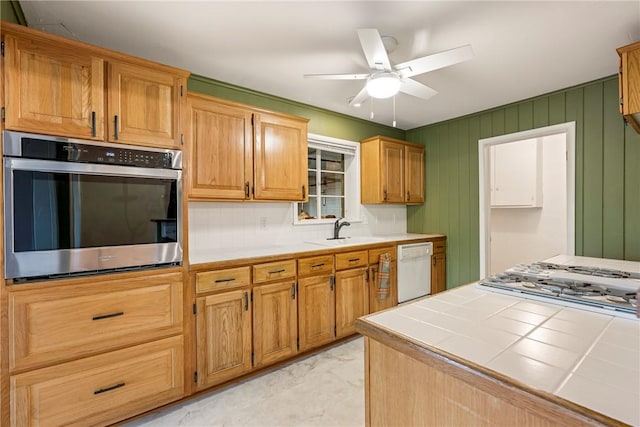 kitchen featuring tile countertops, appliances with stainless steel finishes, a sink, and a ceiling fan