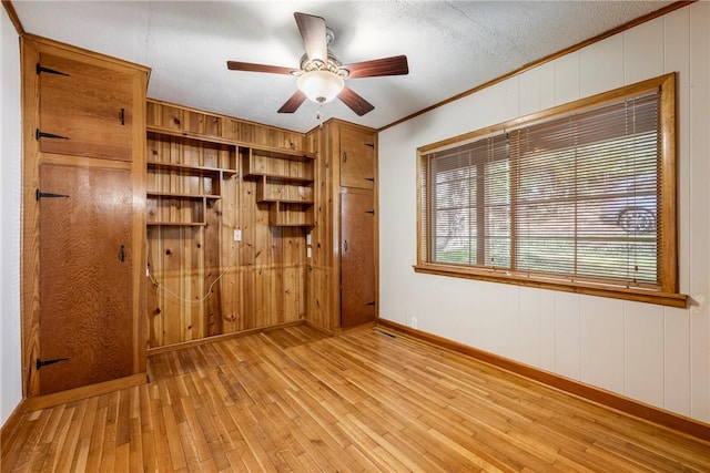 interior space with light wood finished floors, wooden walls, baseboards, ceiling fan, and crown molding