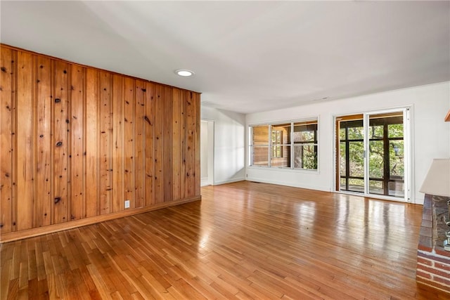 unfurnished living room with baseboards, light wood-style flooring, and wooden walls