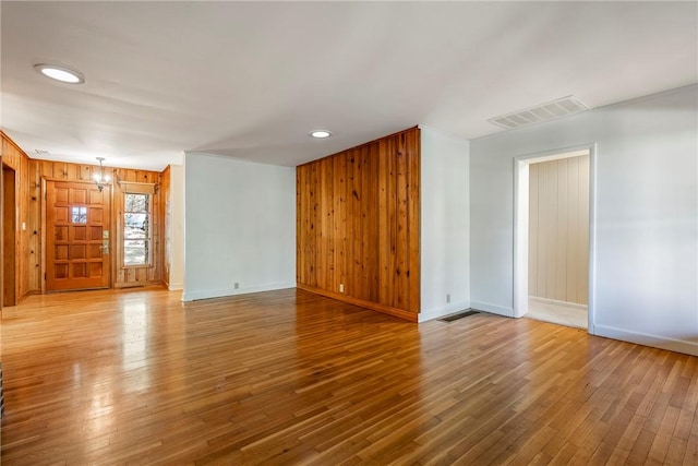 empty room featuring wooden walls, baseboards, visible vents, wood finished floors, and recessed lighting