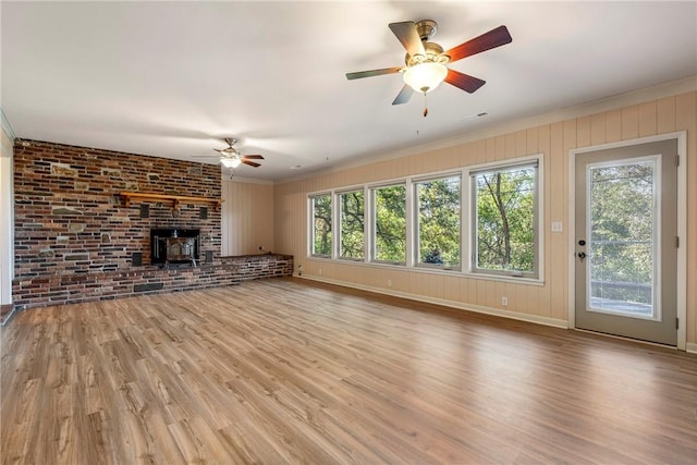 unfurnished living room with a wood stove, light wood-style floors, plenty of natural light, and crown molding