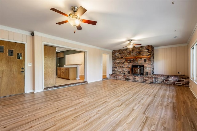 unfurnished living room featuring ceiling fan, ornamental molding, light wood-type flooring, and a wood stove