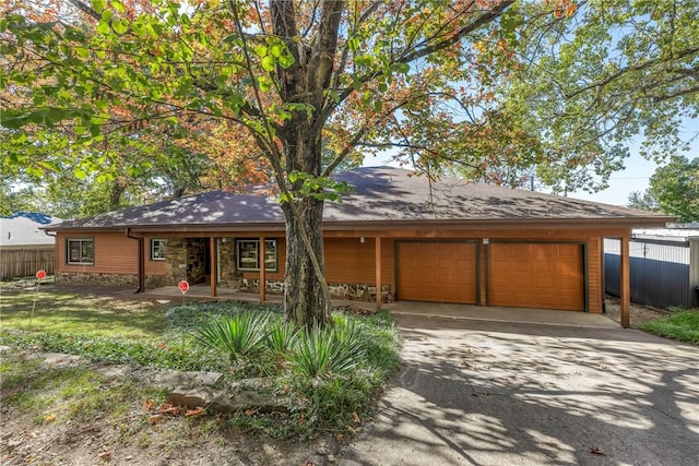 view of front facade with stone siding, an attached garage, fence, and driveway