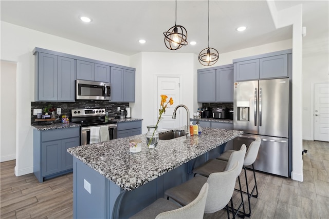 kitchen with light hardwood / wood-style floors, appliances with stainless steel finishes, dark stone counters, and a center island with sink