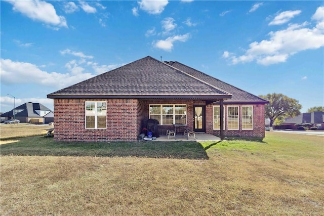 rear view of house featuring a patio, brick siding, roof with shingles, and a lawn