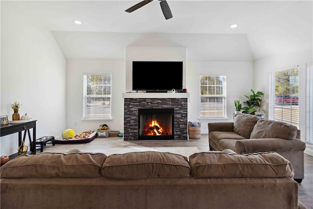 living room featuring a wealth of natural light, lofted ceiling, a stone fireplace, and wood-type flooring