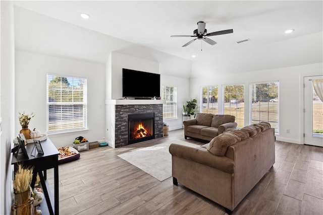 living room with light hardwood / wood-style floors, lofted ceiling, a stone fireplace, and ceiling fan